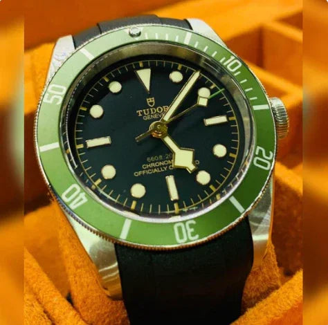 Montre plongeuse Tudor avec lunette verte, cadran noir et bracelet noir, posée dans un écrin orange.